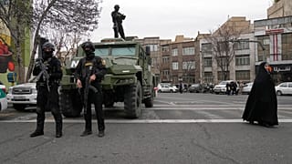 يقف رجال الشرطة على الحراسة خلال التجمع السنوي لإحياء ذكرى الثورة الإسلامية عام 1979، بينما تسير امرأة على اليمين في شارع الحرية (آزادي)، طهران