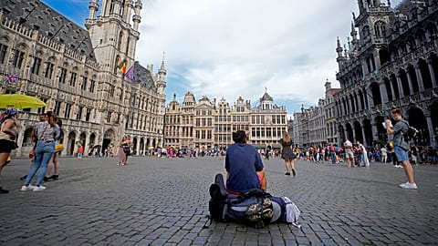 A man sits with his backpack in the center of the historical Grand Place in Brussels on Wednesday, Aug. 24, 2022.