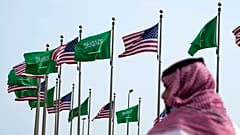 صورة أرشيفية - رجل يقف تحت العلمين الأمريكي والسعودي قبل زيارة الرئيس الأمريكي جو بايدن، في ساحة بجدة، المملكة العربية السعودية
