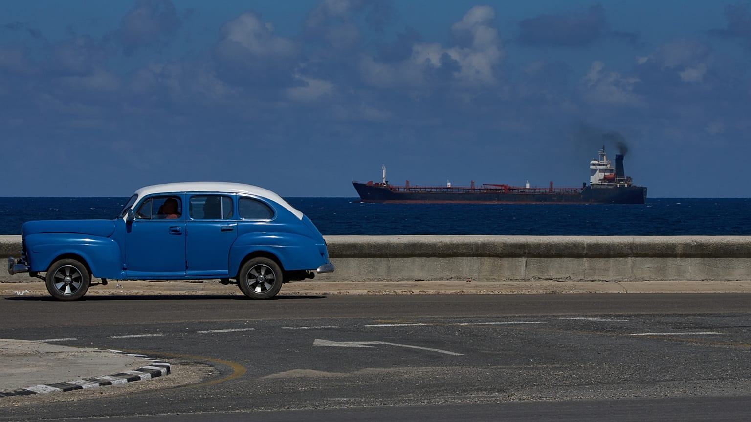 A classic American car drives along the seafront promenade as a tanker exits Havana, Cuba, 