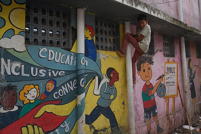 A boy climbs on a pipe next to a wall showing a mural by the Rouble Nagi Art Foundation in the Dhobi Ghat area of Mumbai, India, Thursday, Feb. 5, 2026.