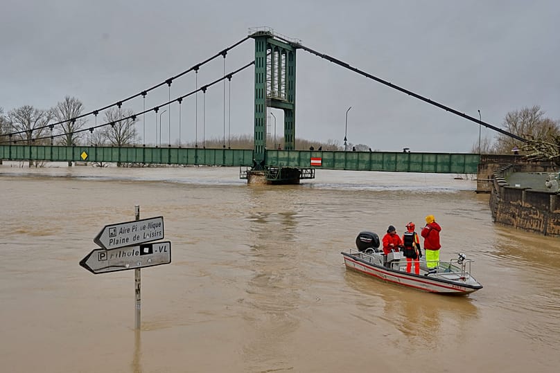 Members of the fire brigades on ride a boat on a flooded road next to a street sign in Marmande, as severe flooding hits western France amid storm Nils, Sunday, Feb. 15, 2026.