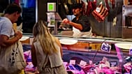 A busy meat market stall with customers interacting with a butcher in Nantes, France.