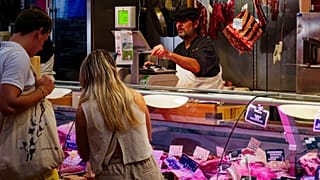 A busy meat market stall with customers interacting with a butcher in Nantes, France.