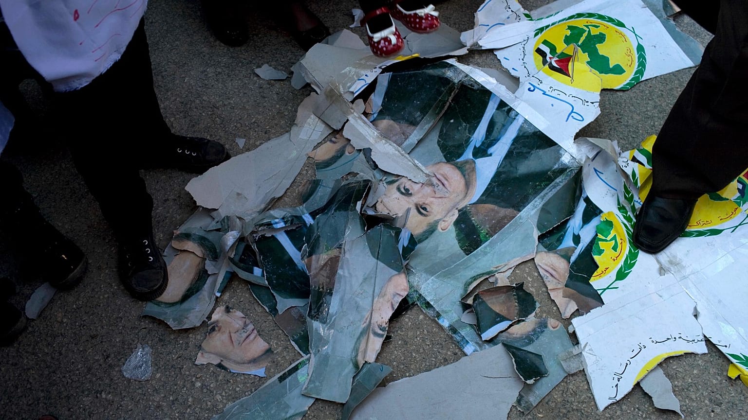 Protesters stand between damaged pictures of Hafez al-Assad, former Syrian president and father of ousted president Bashar al-Assad, during an anti-government protest in a town in northern Syria, Friday, 2 March 2012. 