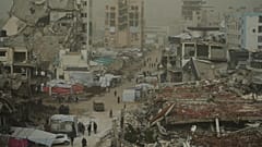 يسير فلسطينيون على طول شارع تحيط به مبانٍ مدمّرة جراء العمليات الجوية والبرية الإسرائيلية خلال عاصفة غبارية في غزة، يوم السبت 14 فبراير/شباط 2026.