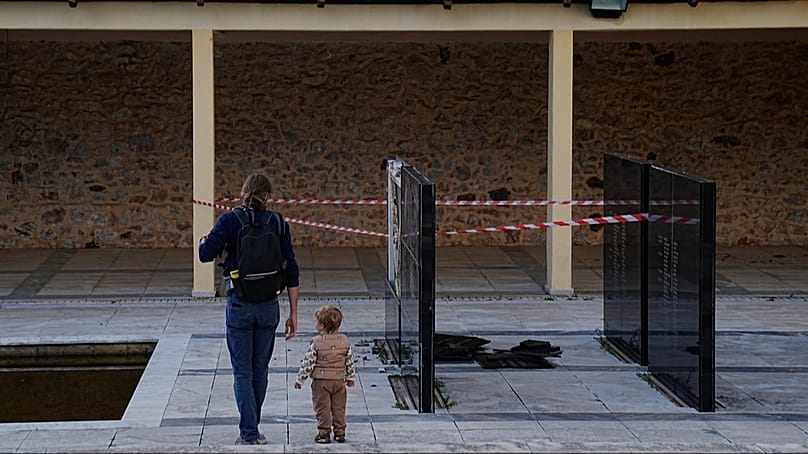 A man with a child walk past a vandalised memorial plaque at the Kaisariani Shooting Range in the Kaisariani suburb of Athens, Greece, 16 Feb, 2026.