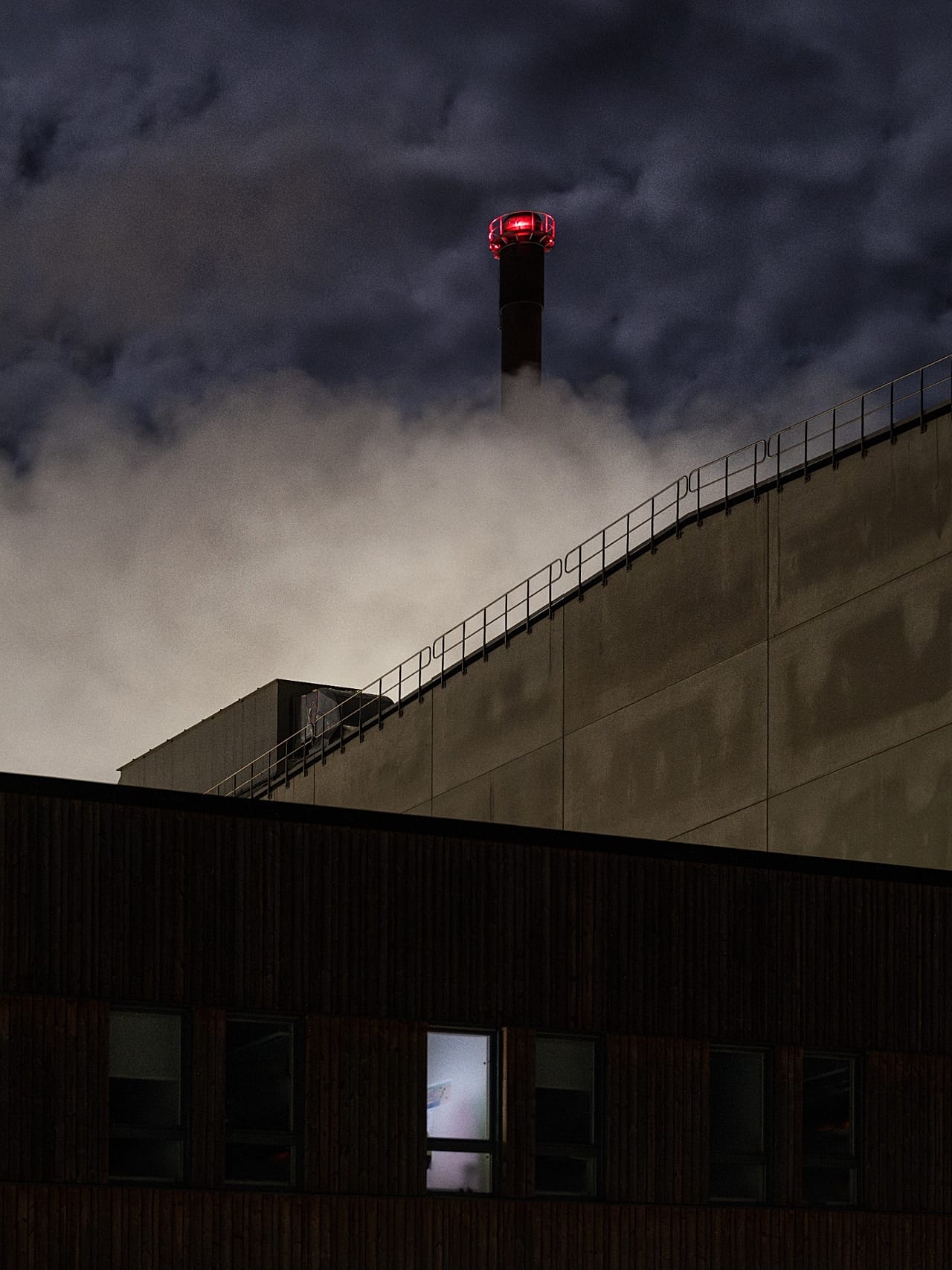 An image of a paper mill in Obbola, Sweden, surrounded by layers of shadows, concrete, and clouds on a dark November night.