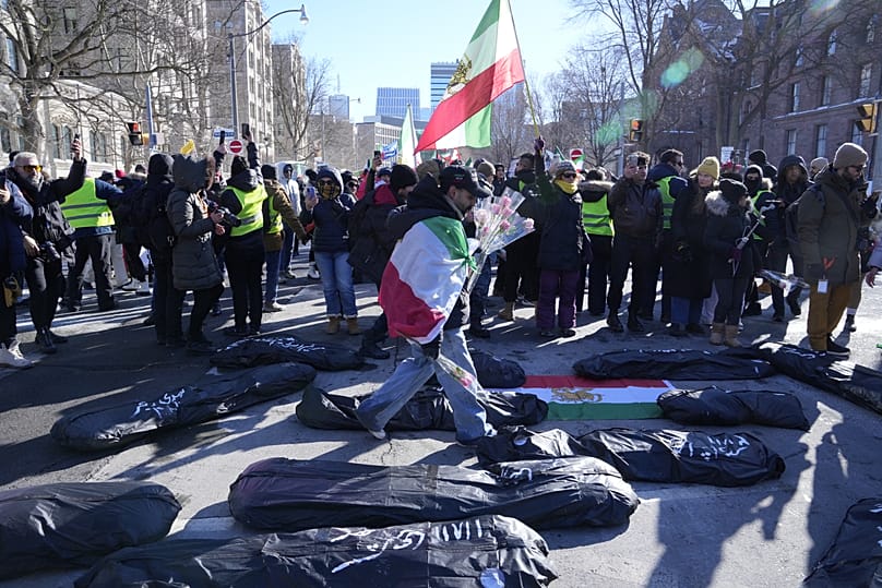 رجل يضع زهورًا على أكياس جثث رمزية دعمًا لتغيير النظام في إيران، خلال تجمع في تورونتو، بتاريخ 1 فبراير 2026.