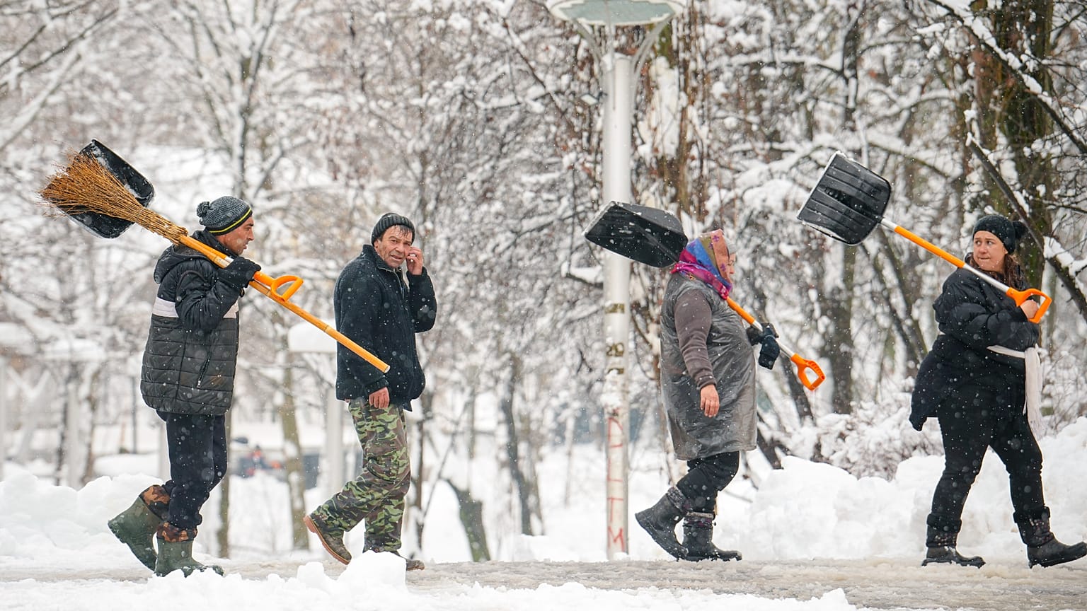 People carrying shovels and brooms walk in a park after a blizzard in Bucharest, Romania, Wednesday, Feb. 18, 2026