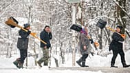 Des personnes portant des pelles et des balais se promènent dans un parc après un blizzard à Bucarest, en Roumanie, le mercredi 18 février 2026.