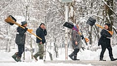 In Bukarest in Rumänien gehen Menschen mit Schaufeln und Besen durch einen Park. Zuvor hatte ein Schneesturm gewütet, am Mittwoch, 18. Februar 2026.