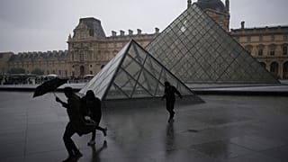 يهرب الناس من المطر في فناء متحف اللوفر خلال هطول الأمطار يوم الاثنين 27 أكتوبر/تشرين الأول 2025 في باريس. (صورة من وكالة أسوشيتد برس/كريستوف إينا)