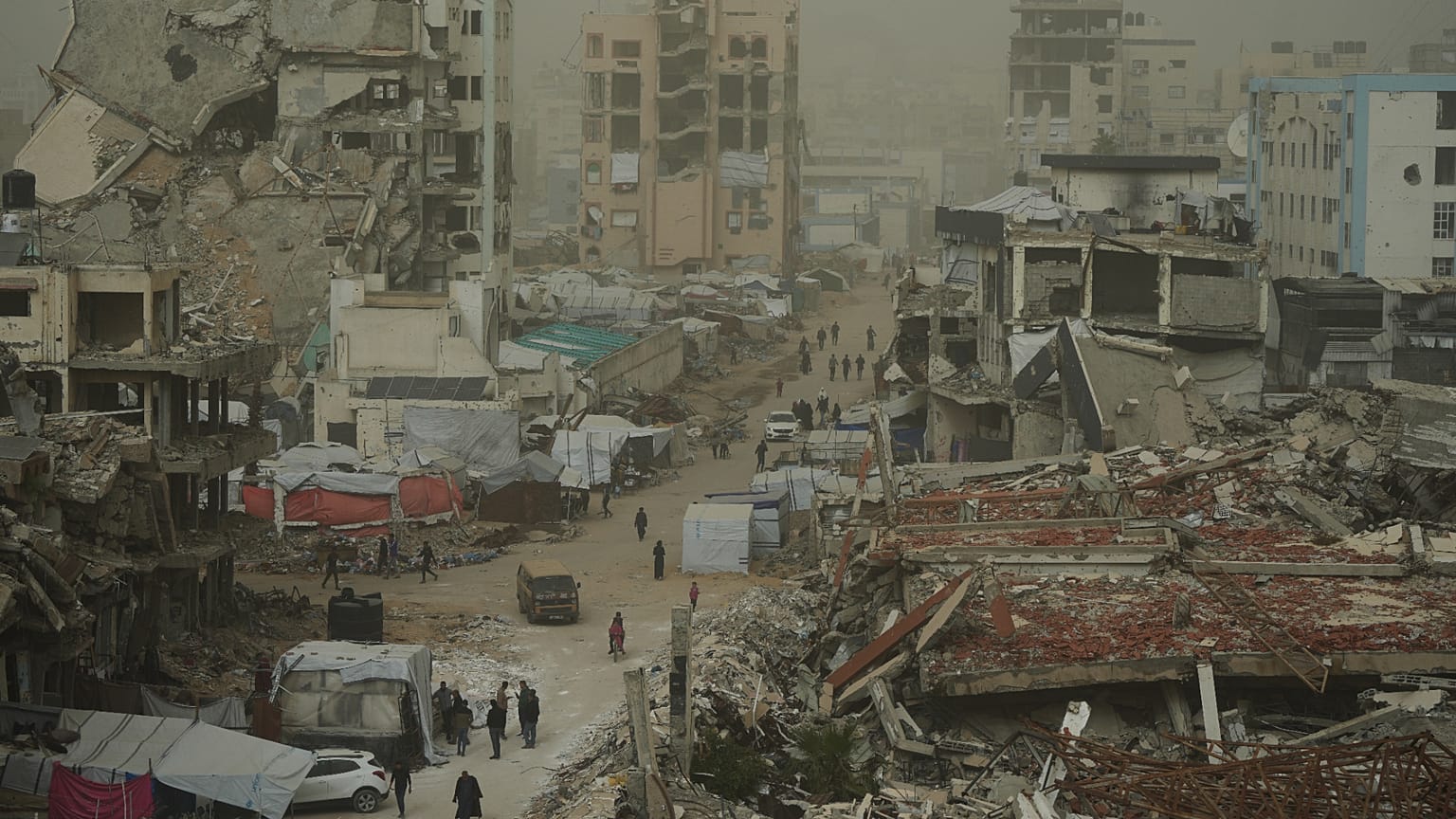 Filistinliler, 14 Şubat 2026 Cumartesi günü Gazze şehrinde, İsrail'in hava ve kara operasyonlarında yıkılan binalarla çevrili bir sokakta, toz fırtınası sırasında yürüyorlar.