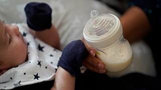 FILE: A woman holds a bottle of baby formula as she feeds her infant son, Friday, May 13, 2022, in San Antonio.