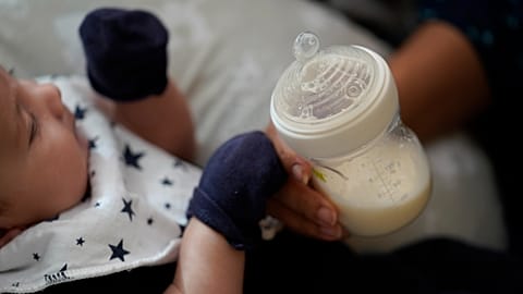 FILE: A woman holds a bottle of baby formula as she feeds her infant son, Friday, May 13, 2022, in San Antonio.