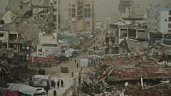 فلسطينيون يسيرون على طول شارع محاط بمباني دمرت في العمليات الجوية والبرية الإسرائيلية خلال عاصفة ترابية في مدينة غزة, السبت, فبراير. 14, 2026.