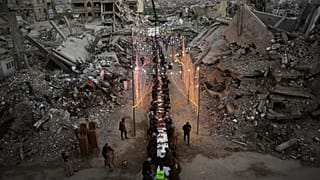 يجلس فلسطينيون حول مائدة طويلة وسط أنقاض مبانٍ مدمّرة، أثناء تجمعهم لتناول وجبة الإفطار، في شهر رمضان، في مدينة خان يونس بقطاع غزة، الخميس 19 فبراير/شباط 2026. 