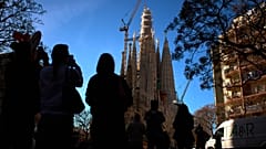 Varias personas observan cómo una grúa eleva el brazo superior de la cruz sobre la Torre de Jesucristo en la Sagrada Familia de Barcelona, España