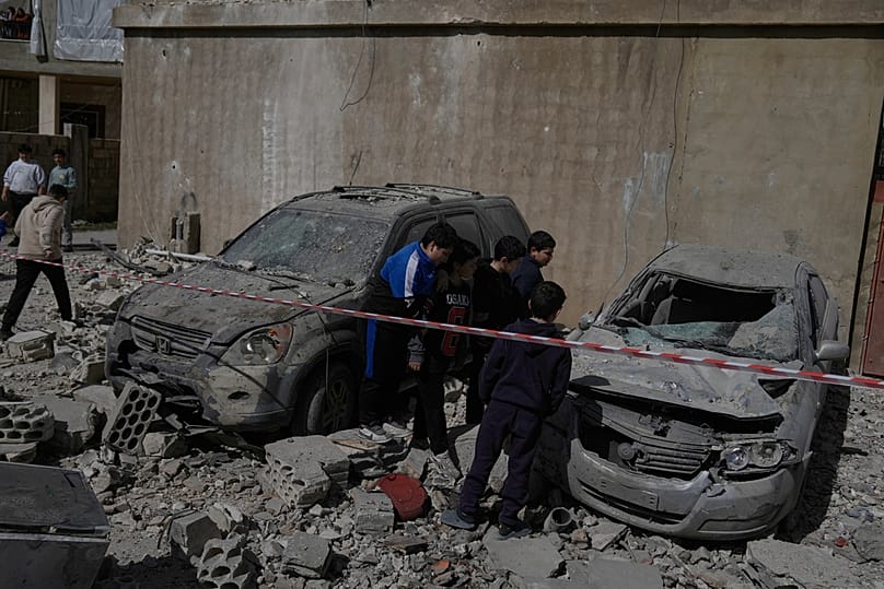 People inspect damaged cars near a building destroyed in an Israeli strike in the village of Temnine in eastern Lebanon, Saturday, Feb. 21, 2026
