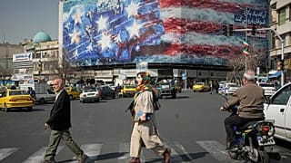 Pedestrians walk past a billboard depicting a U.S. aircraft carrier with damaged fighter jets on its deck in Tehran, Iran, Sunday, Feb. 22, 2026.