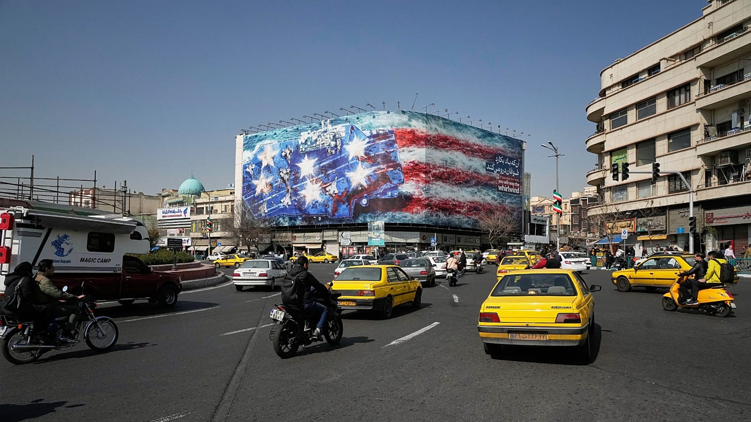 Vehicles pass a billboard depicting a US aircraft carrier with damaged fighter jets on its deck at Enqelab-e-Eslami (Islamic Revolution) Square in Tehran, Iran, Feb. 22, 2026.