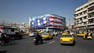 Vehicles pass a billboard depicting a US aircraft carrier with damaged fighter jets on its deck at Enqelab-e-Eslami (Islamic Revolution) Square in Tehran, Iran, Feb. 22, 2026.