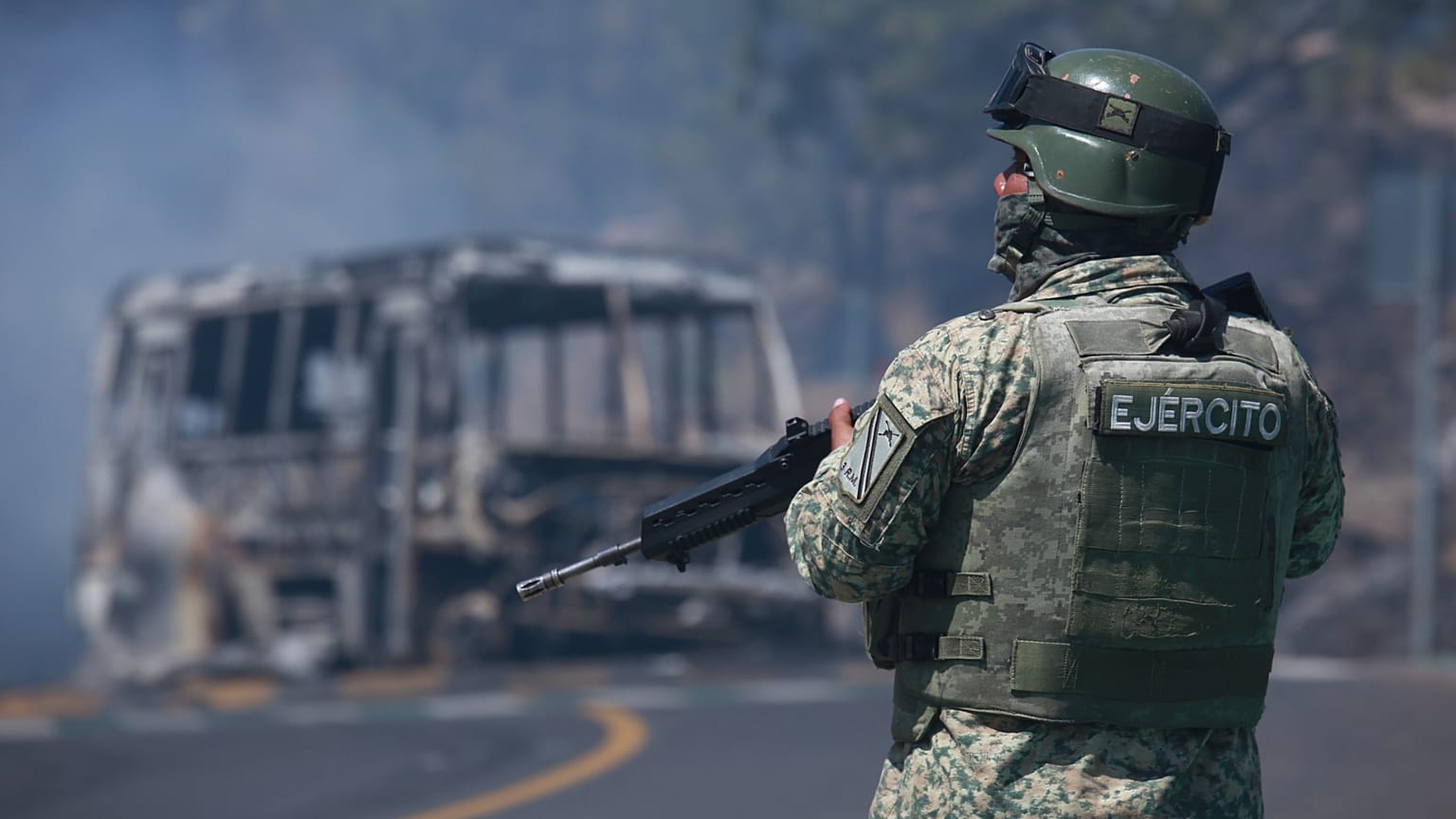 A soldier stands guard by a charred vehicle after it was set on fire in Cointzio, Michoacán state, Mexico, Sunday, Feb. 22, 2026.