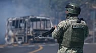 A soldier stands guard by a charred vehicle after it was set on fire in Cointzio, Michoacán state, Mexico, Sunday, Feb. 22, 2026.