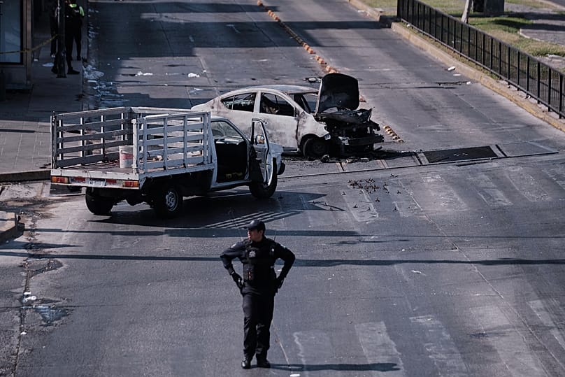 A police officer stands guard by a charred vehicle after it was set on fire, on a road in Guadalajara, Jalisco state, Mexico, Sunday, Feb. 22, 2026.