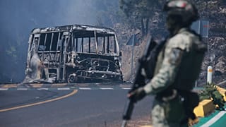 A soldier stands guard by a charred vehicle after it was set on fire, in Cointzio, Michoacán state, following the death of the leader of the Jalisco New Generation Cartel