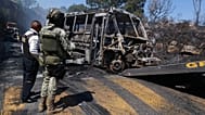 A soldier stands guard by a charred vehicle that was set on fire in Cointzio, 22 Februar 2026