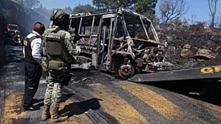 A soldier stands guard by a charred vehicle that was set on fire in Cointzio, 22 Februar 2026