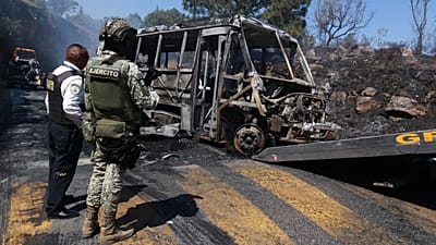 A soldier stands guard by a charred vehicle that was set on fire in Cointzio, 22 Februar 2026