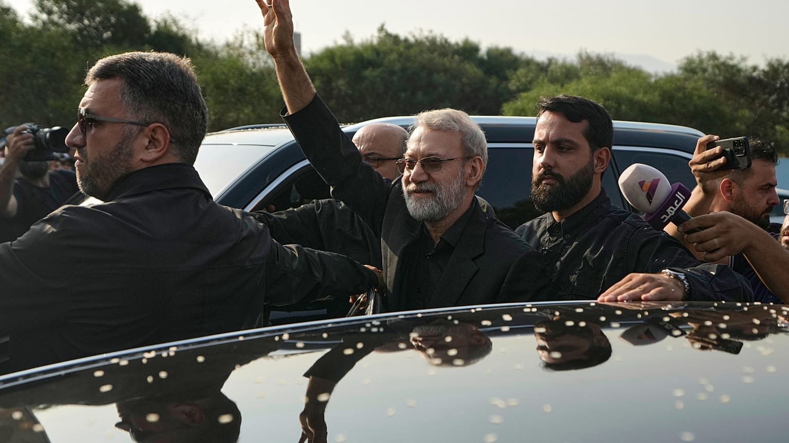 علي لاريجاني يلوّح لأنصار حزب الله لدى وصوله إلى مطار رفيق الحريري في بيروت، 13 أغسطس/آب 2025.