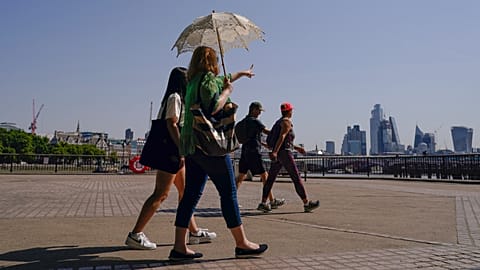 A woman holds an umbrella to shelter from the sun, as she walks on the south bank of river Thames, in London, Monday, July 18, 2022. 