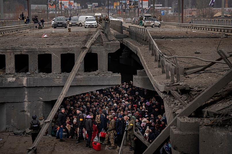 Ukrainians crowd under a destroyed bridge as they try to flee by crossing the Irpin River on the outskirts of Kyiv, Ukraine, Saturday, March 5, 2022. 