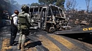 A soldier stands guard by a charred vehicle that was set on fire in Cointzio, Mexico, Sunday, Feb. 22, 2026.