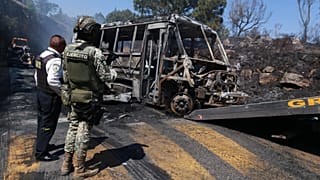 A soldier stands guard by a charred vehicle that was set on fire in Cointzio, Mexico, Sunday, Feb. 22, 2026.