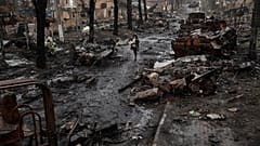 DATEI. Eine Frau geht durch eine mit Trümmern übersäte Straße, auf der zerstörte russische Militärfahrzeuge stehen, in Bucha am Stadtrand von Kiew, Ukraine, Apr. 2022