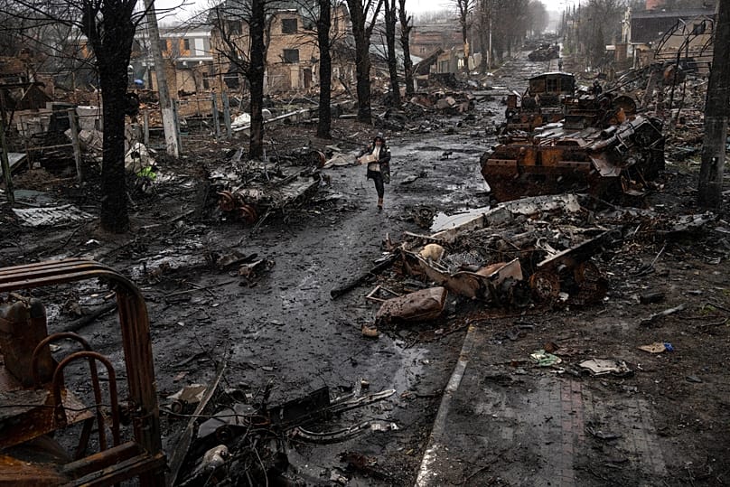 A woman navigates a debris-filled street where destroyed Russian military vehicles stand in Bucha on the outskirts of Kyiv, 3 April, 2022