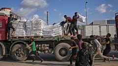 فلسطينيون يحصلون على أكياس طحين من شاحنة مساعدات تابعة لبرنامج الأغذية العالمي أثناء مرورها في دير البلح وسط قطاع غزة، في 15 نوفمبر 2025.
