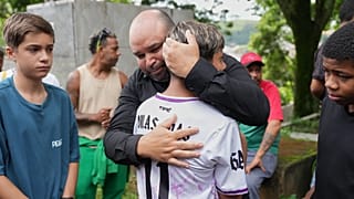 Отец 11-летнего мальчика, погибшего из-за сильных дождей и наводнения, получает поддержку друзей сына на его похоронах в Жуис-ди-Фора.