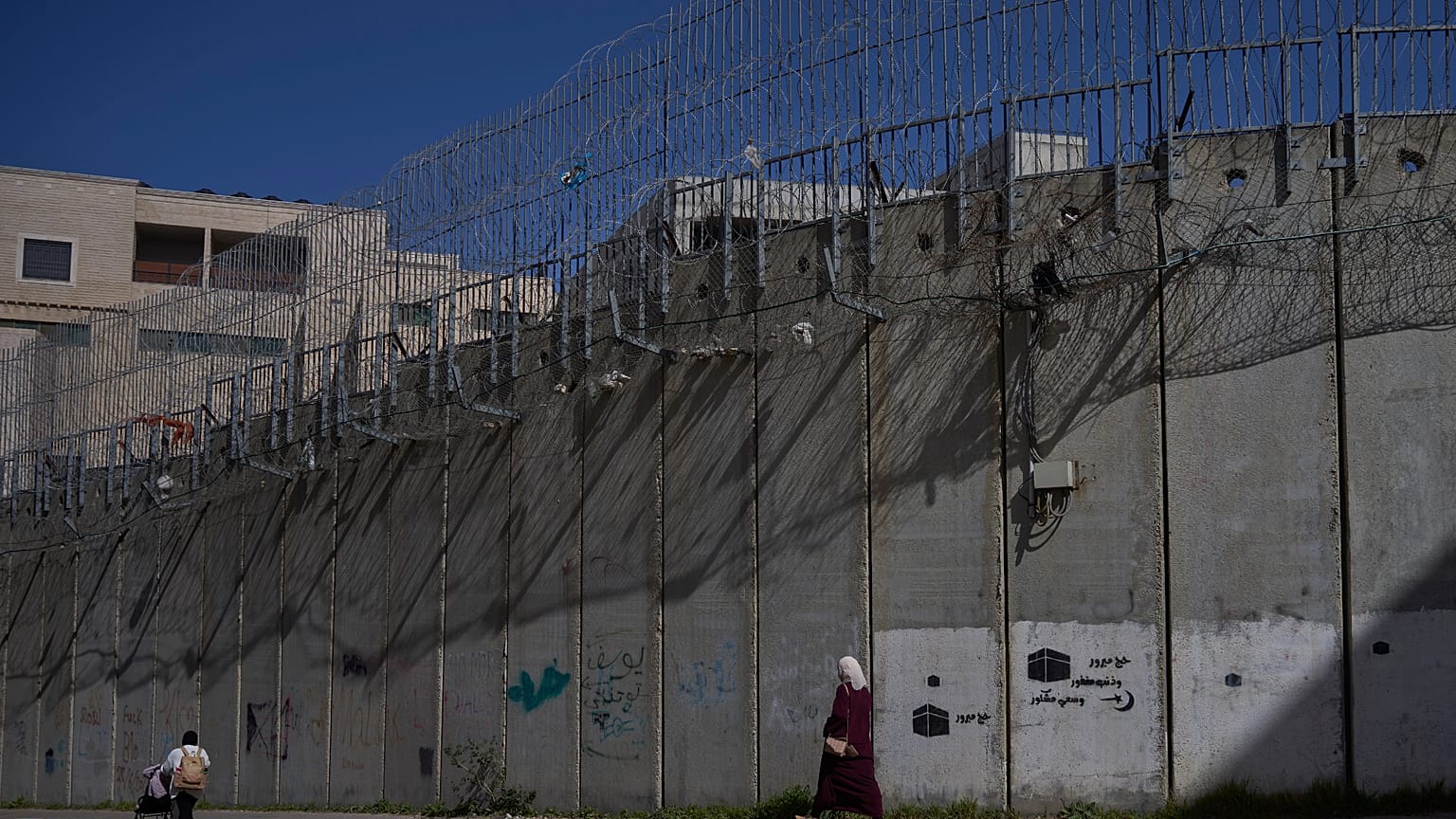 فلسطينيون يسيرون على طول جدار الفصل بين الضفة الغربية وحي بيت حنينا في القدس الشرقية، الأحد 15 فبراير 2026. (صورة من وكالة أسوشيتد برس/أوهاد زويجنبرغ)