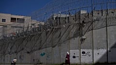 فلسطينيون يسيرون على طول جدار الفصل بين الضفة الغربية وحي بيت حنينا في القدس الشرقية، الأحد 15 فبراير 2026. (صورة من وكالة أسوشيتد برس/أوهاد زويجنبرغ)