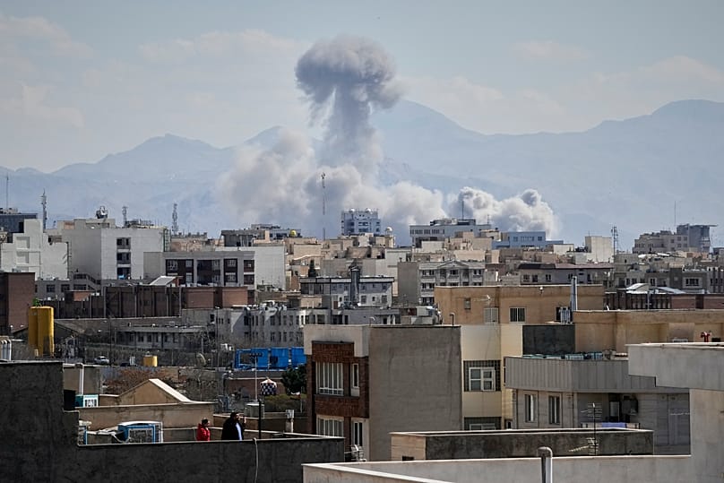 People watches from rooftop as a plume of smoke rises after a strike in Tehran, Iran, Sunday, March 1, 2026.