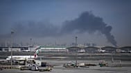 A plume of smoke caused by an Iranian strike is seen in the background as Emirates planes are parked at Dubai International Airport after its closure