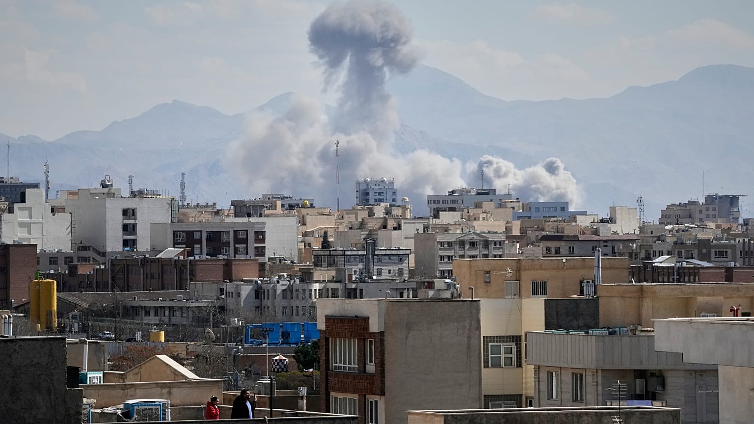 La gente osserva da un tetto mentre una colonna di fumo si alza dopo uno sciopero a Teheran, Iran, domenica 1 marzo 2026. (Foto AP/Vahid Salemi)