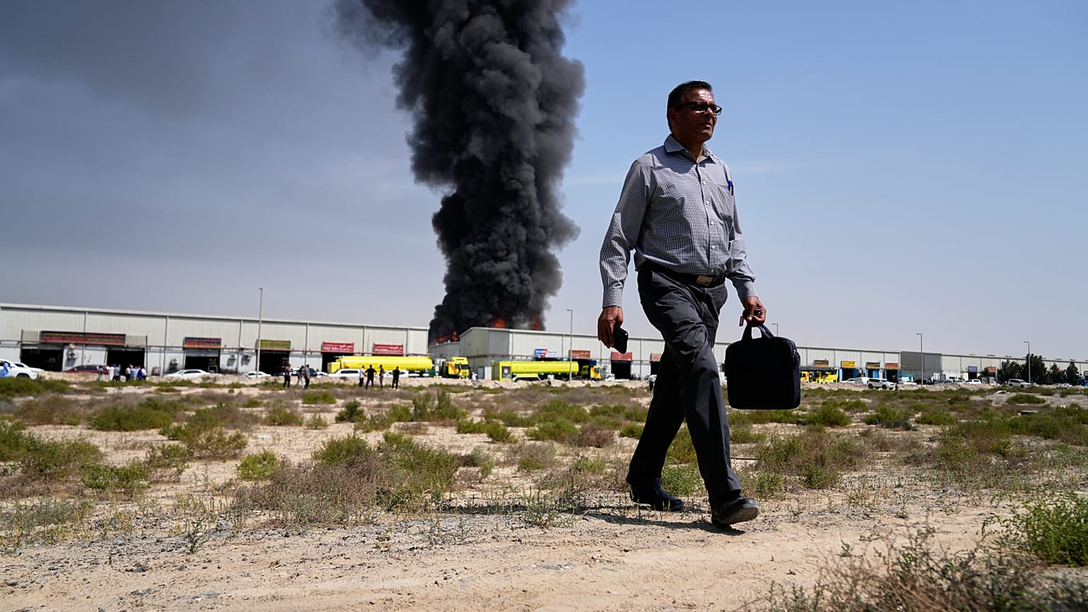 A man walks away after watching as a black plume of smoke rises from a warehouse in the industrial area of Sharjah City, United Arab Emirates, Sunday, March 1, 2026, following