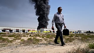 A man walks away after watching as a black plume of smoke rises from a warehouse in the industrial area of Sharjah City, United Arab Emirates, Sunday, March 1, 2026, following